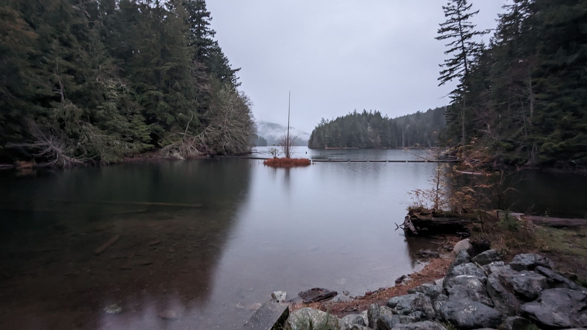 A serene lake surrounded by dark forests under an overcast sky. - Little Summit – Mount Constitution loop from Little Summit