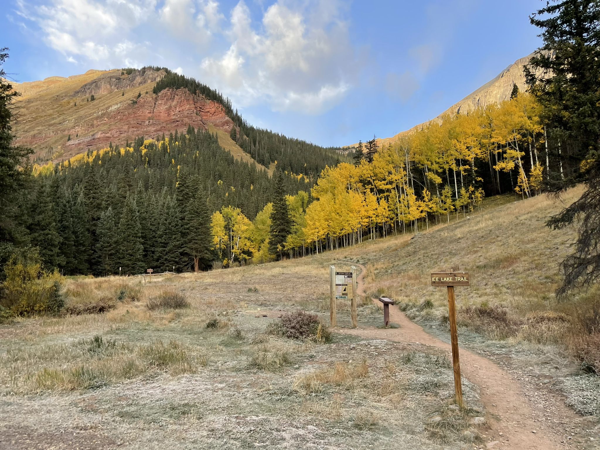 Trail signs in a frosty meadow with golden aspen trees and mountains. - Clear Lake Trail