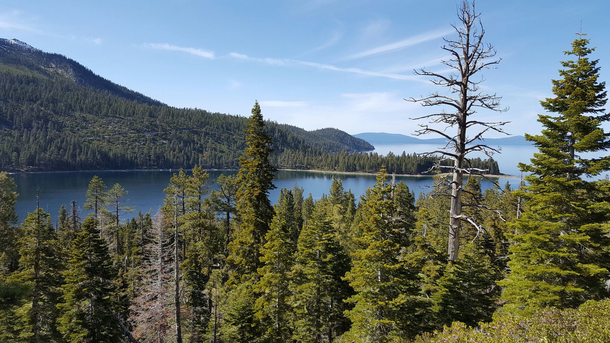 Dense pine forest framing a serene lake with distant mountains under a blue sky. - Nice Beach in the Emerald Bay – Lower Eagle Falls loop from Emerald Bay State Park