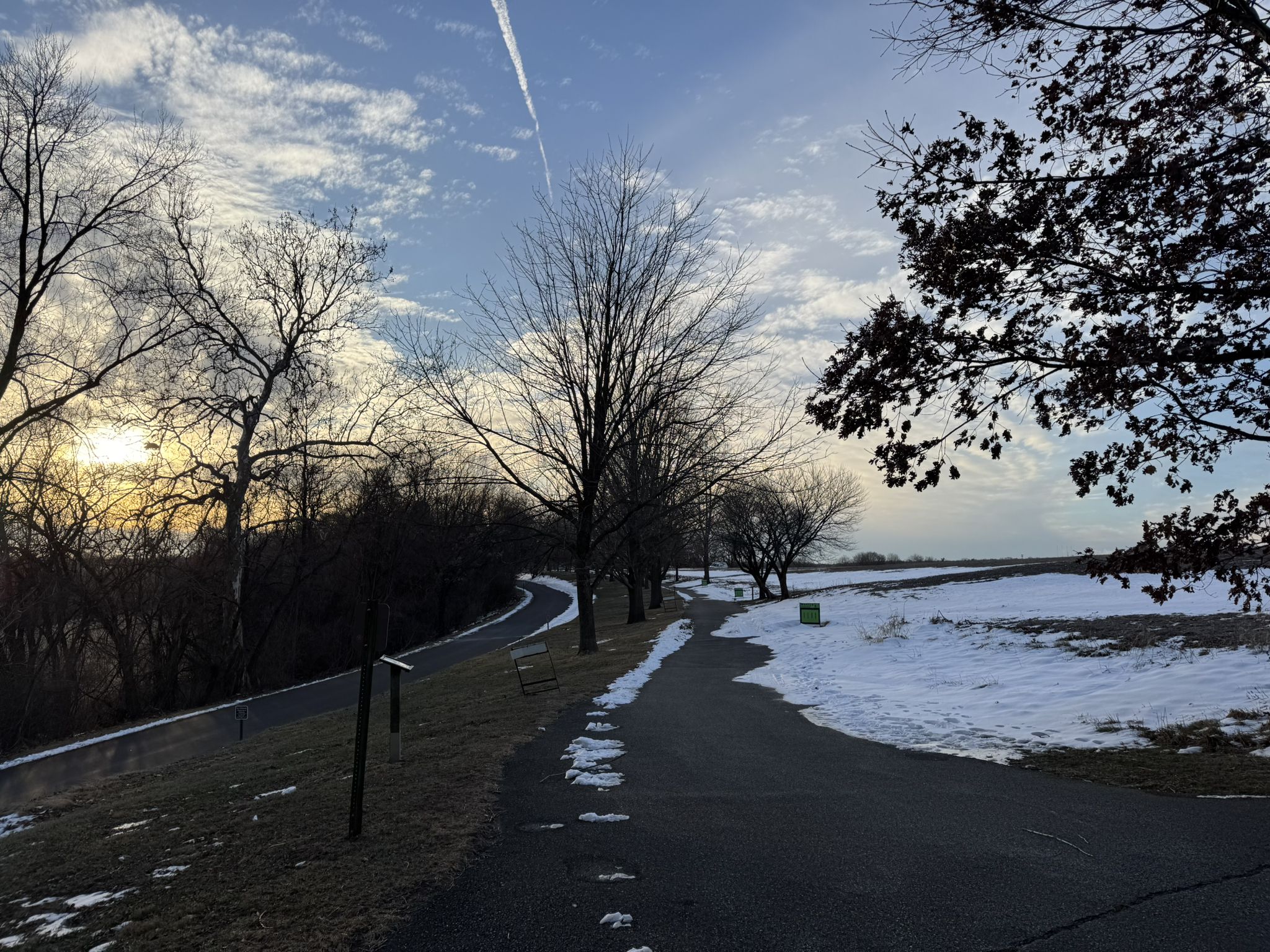 Paved path with snow patches, bare trees, and a colorful sunset sky. - Farm Park Trail Loop