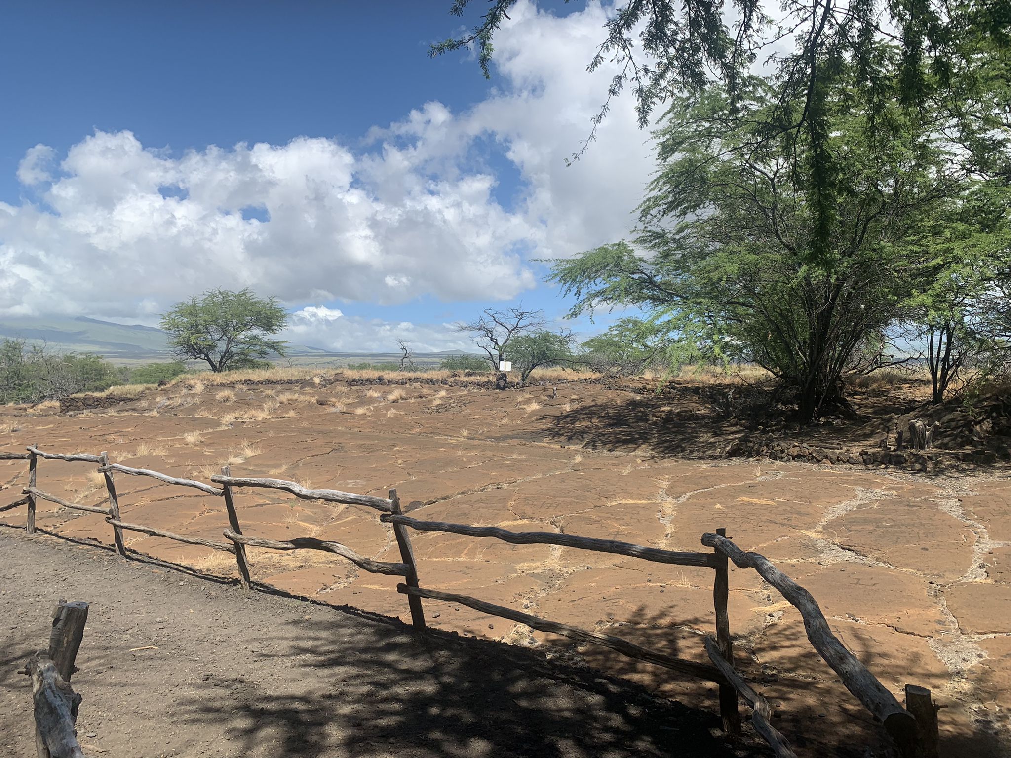 Rustic wooden fence bordering a large, flat rocky area under a bright, cloudy sky. - Puakō Petroglyph Field loop from 49 Black Sand Beach