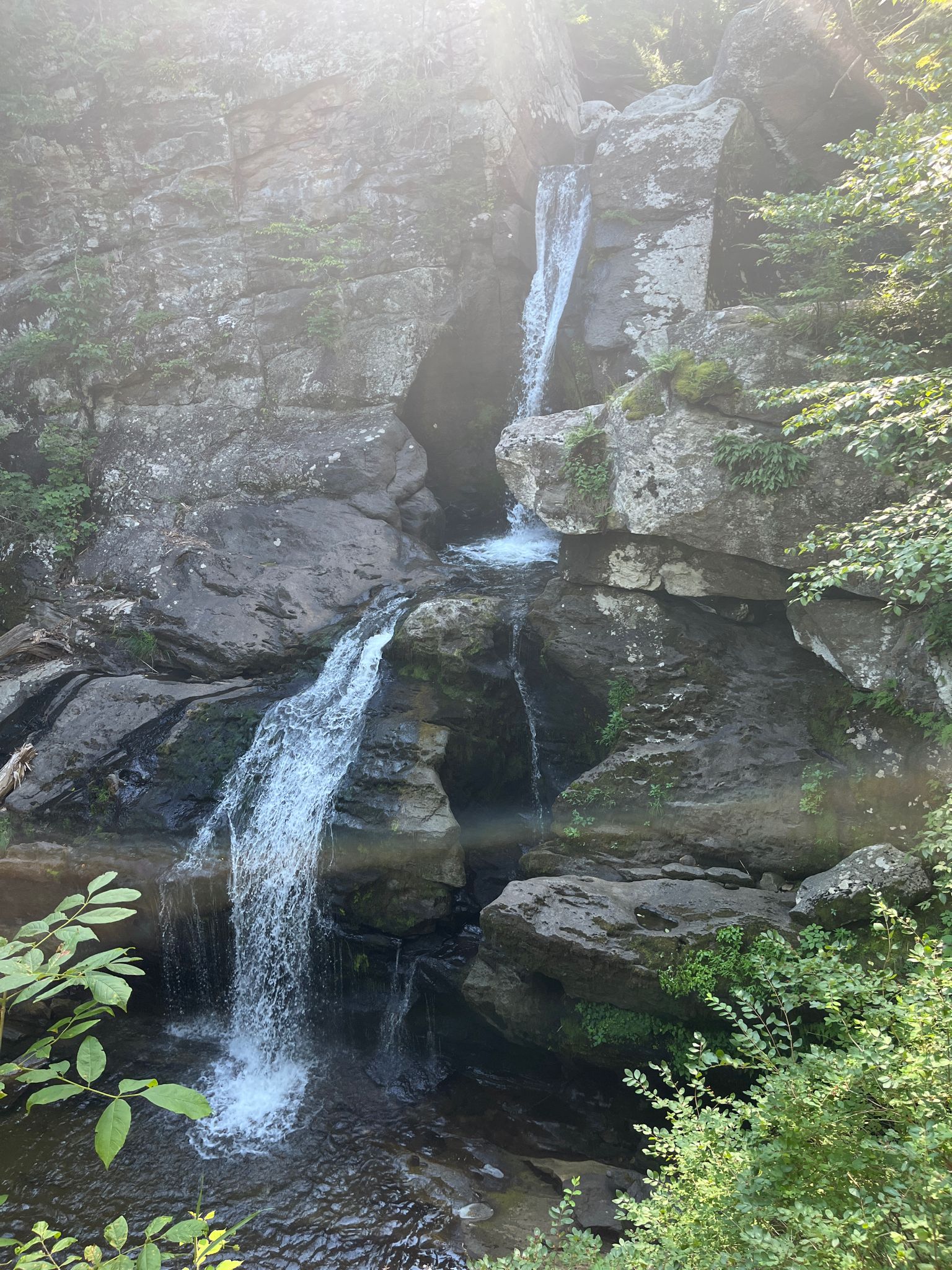 Sunlight illuminates a waterfall cascading over dark, rugged rock cliffs. - Kent Falls Red and Yellow Loop Trail