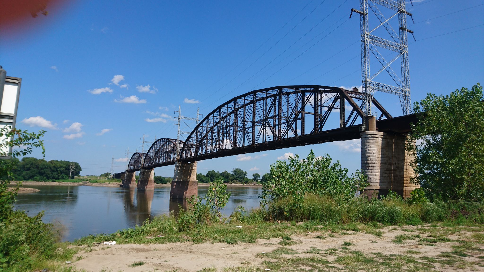 An arched metal truss bridge spans a river with power lines overhead. - The Grand Basin, Forest Park – Grand Drive loop from Florissant