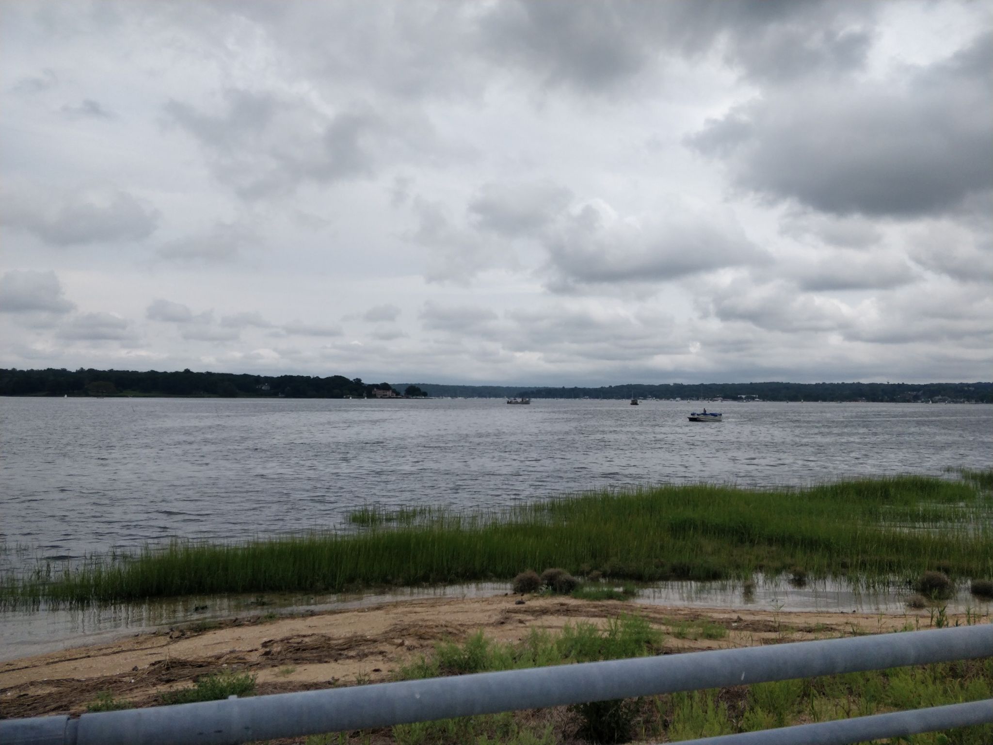 Overcast view of a wide bay with boats, marsh grass, and distant treeline. - West Shore Road