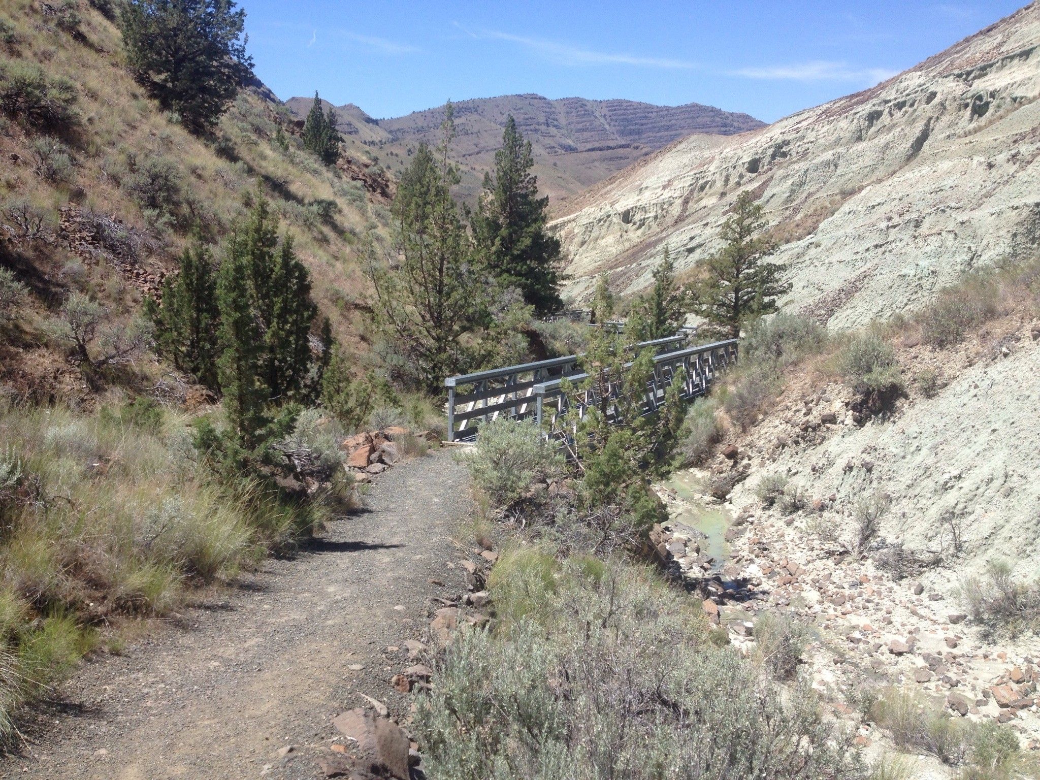 Dirt path leading to a wooden bridge in a rocky canyon under clear sky. - Blue Basin loop from Blue Basin