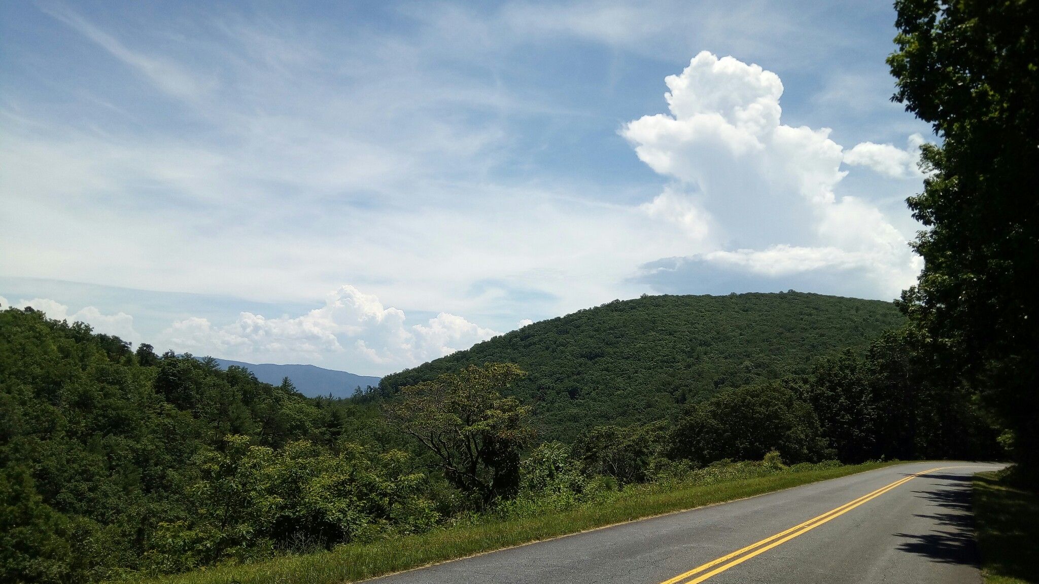 A winding road through green mountains under a bright, partly cloudy sky. - Natural Bridge of Virginia – Caverns at Natural Bridge loop from The Pinnacle