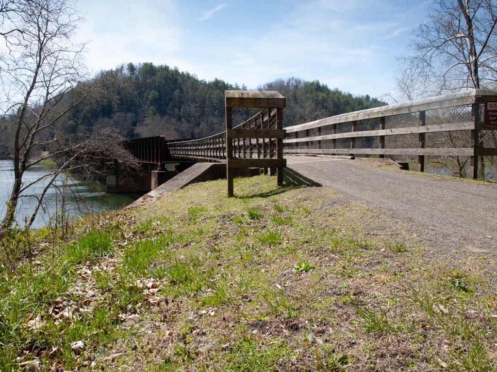 Wooden bridge extending over a river, with grassy banks and hills. - New River Trail: Fries Section