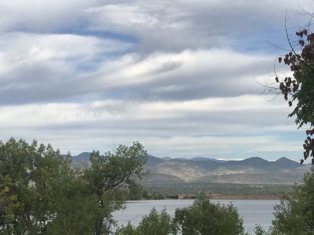 Lake with distant mountains, framed by green trees under a cloudy sky. - High Line Canal, Lee Gulch, and Mineral Ave. Trail