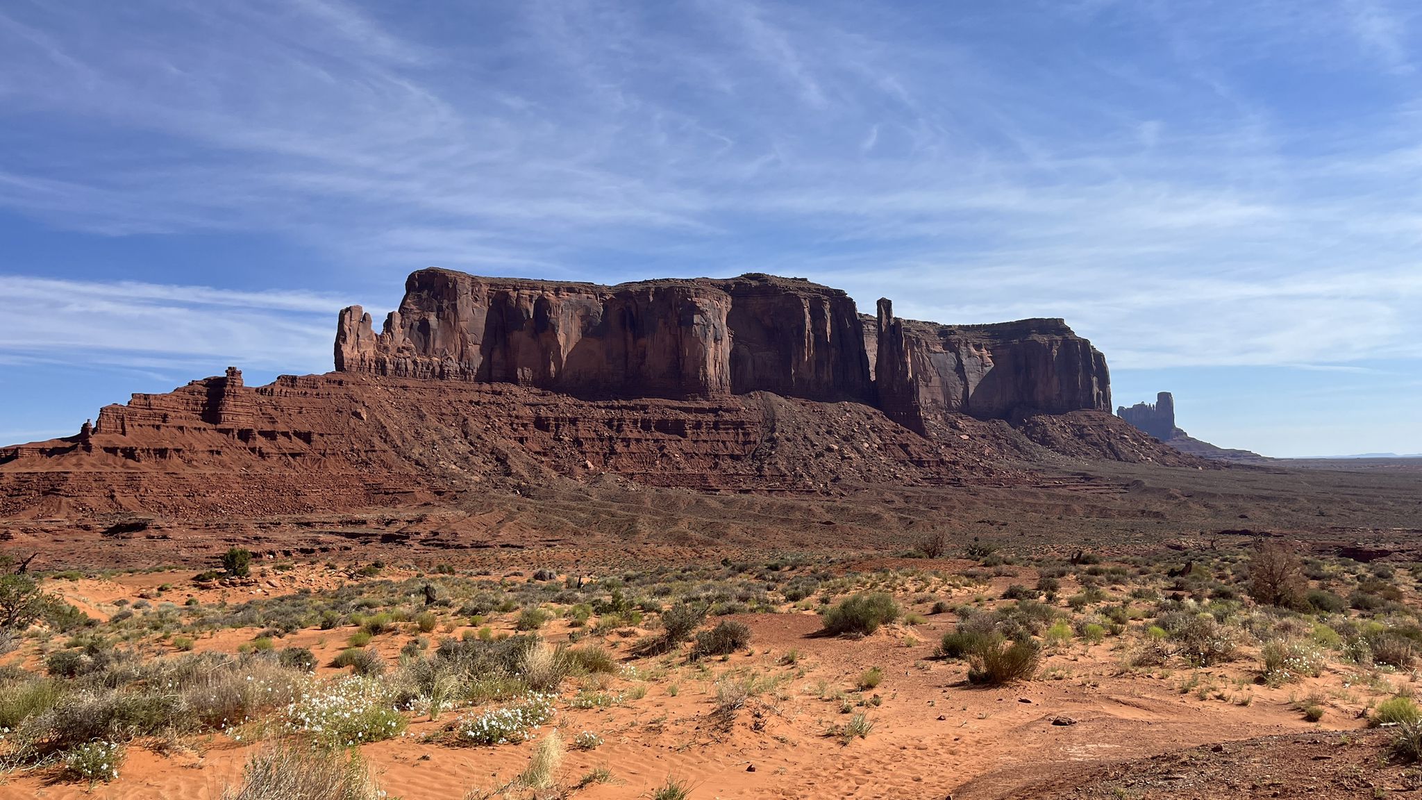 Expansive desert with a long red rock mesa under a blue sky with wispy clouds. - Great view of Monument Valley loop from Monument Valley Navajo Tribal Park