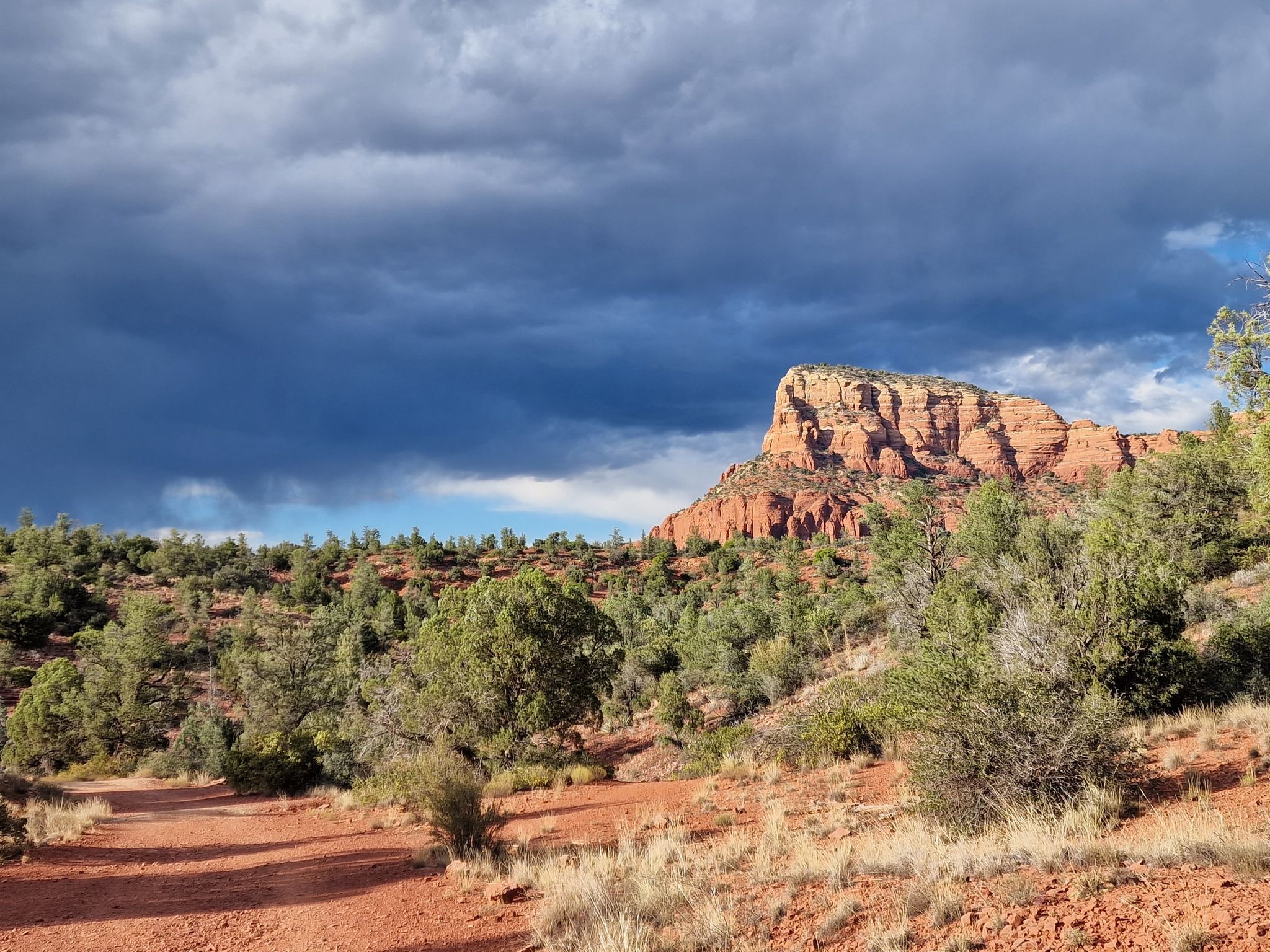 Red rock mountain under dramatic cloudy sky, with a dirt path. - Courthouse Butte and Bell Rock Loop