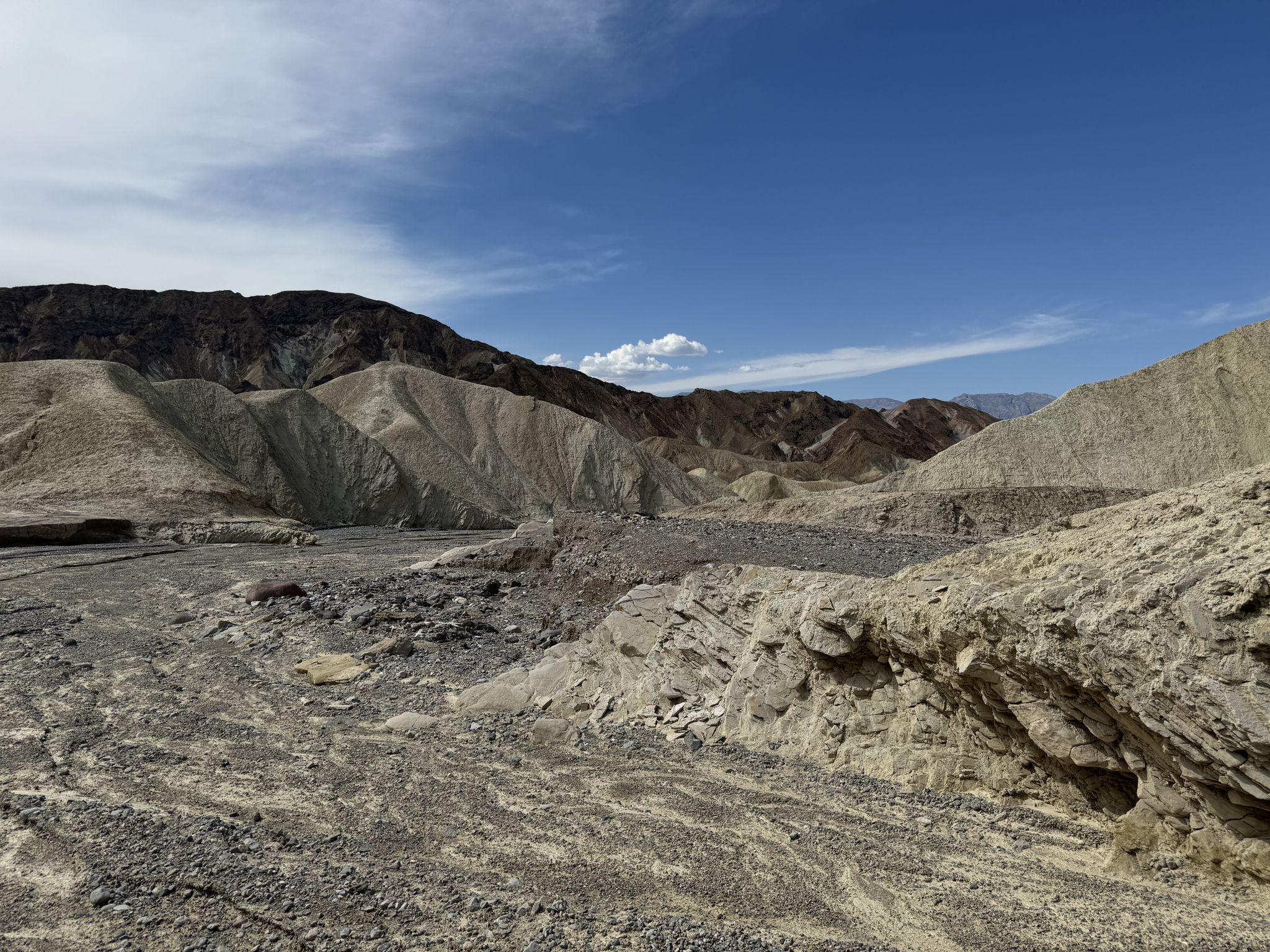 Wide desert wash with rocky terrain and distant mountains under blue sky. - Badlands Loop