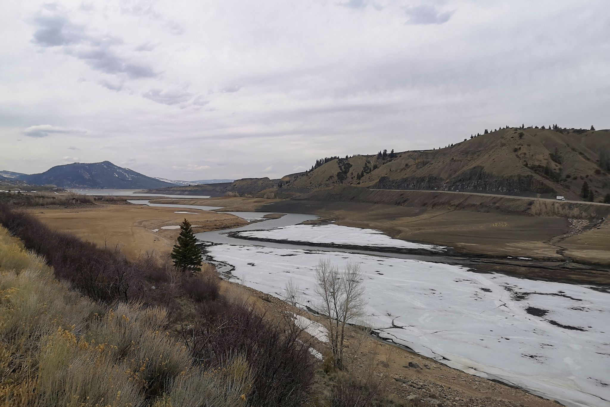 A partially frozen river winding through dry banks and distant mountains. - Green Mountain Reservoir Loop