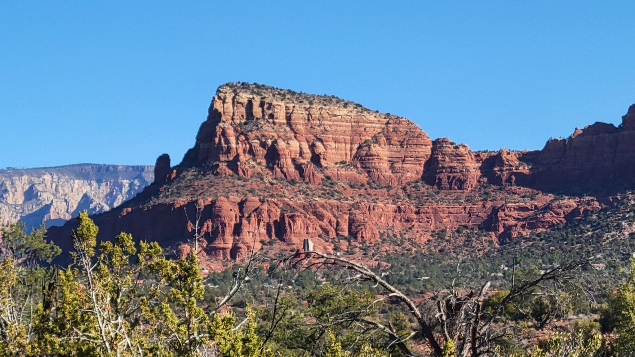 Large red rock mountain with distant cliffs under a clear blue sky. - Llama to Made in the Shade – MTB Trails in Sedona