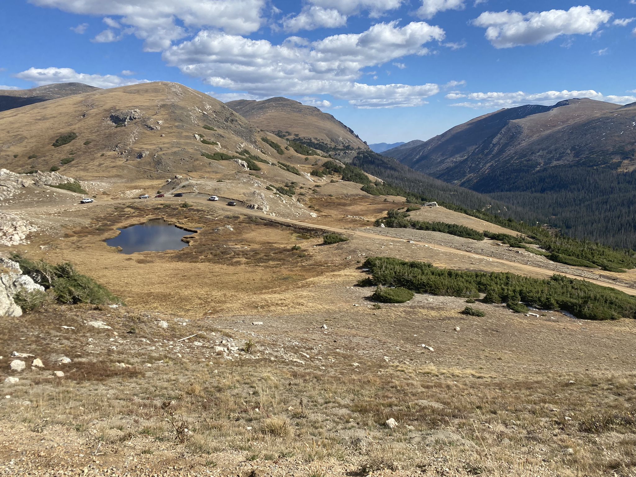 An expansive high-altitude landscape with a small pond, sparse vegetation, and distant mountains. - Marmot Point loop from Alpine Visitor Center