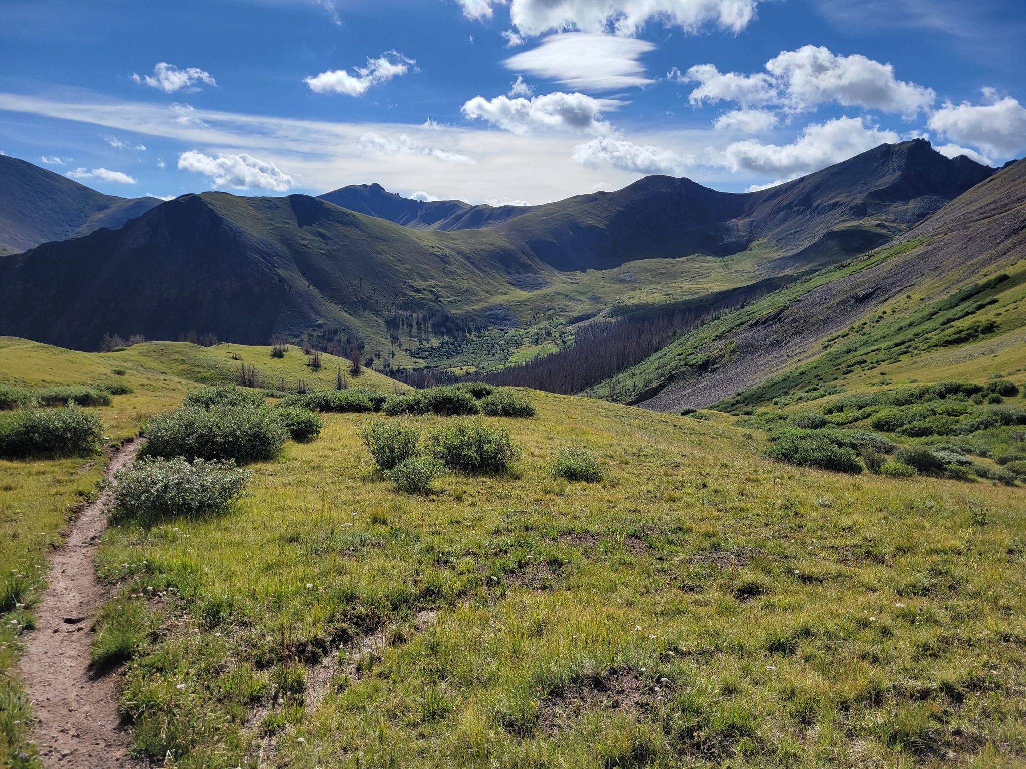 A winding dirt trail through a green mountain valley under a cloudy sky. - San Luis Peak - South Ridge