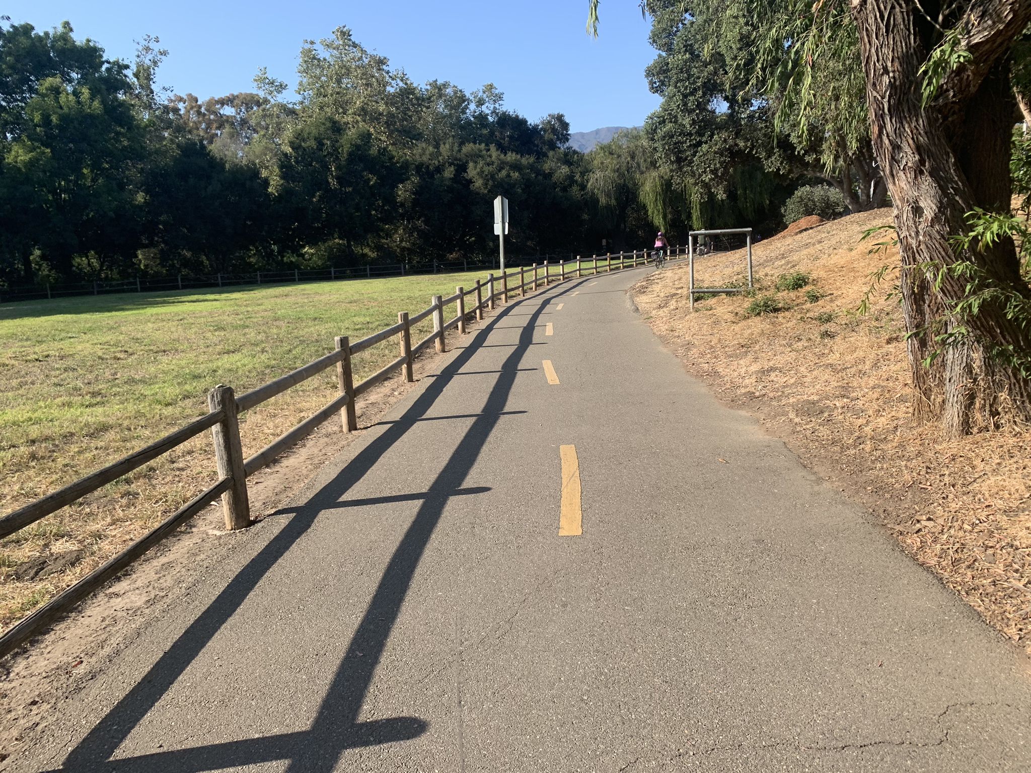 Paved path with wooden fence, green field, and distant mountains. - Atascadero Creek dirt trail loop from San Marcos High School
