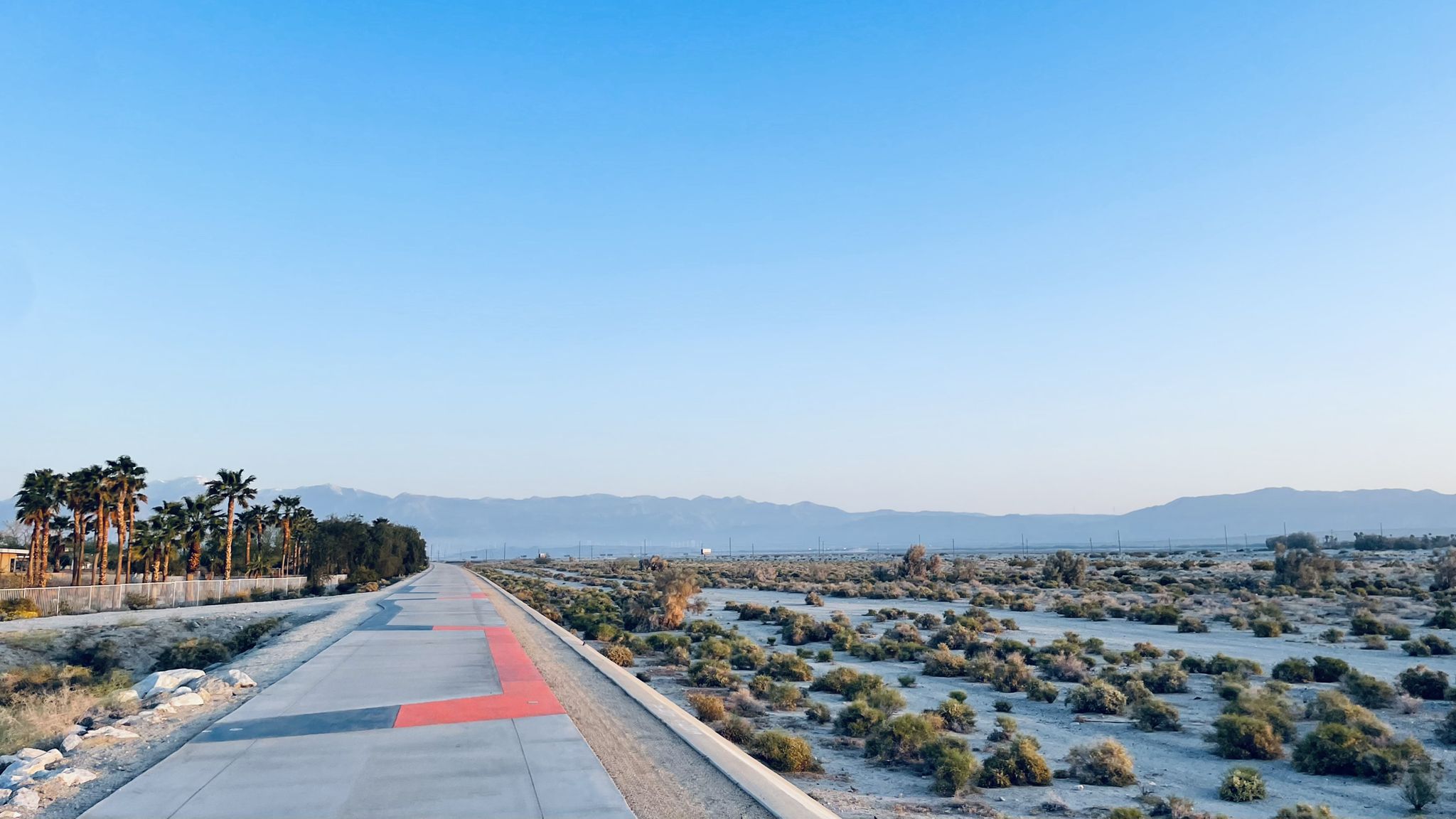 Paved path through desert scrubland with distant mountains under a clear sky. - CV Link
