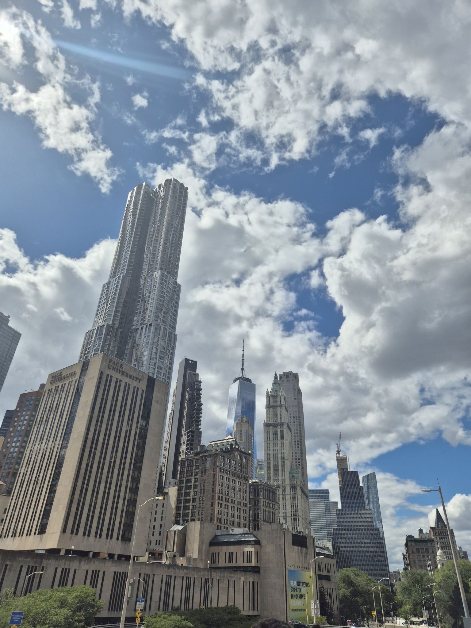 Upward view of towering skyscrapers against a bright blue sky with white clouds. - New York Stock Exchange – New York City Hall loop from Wall Street