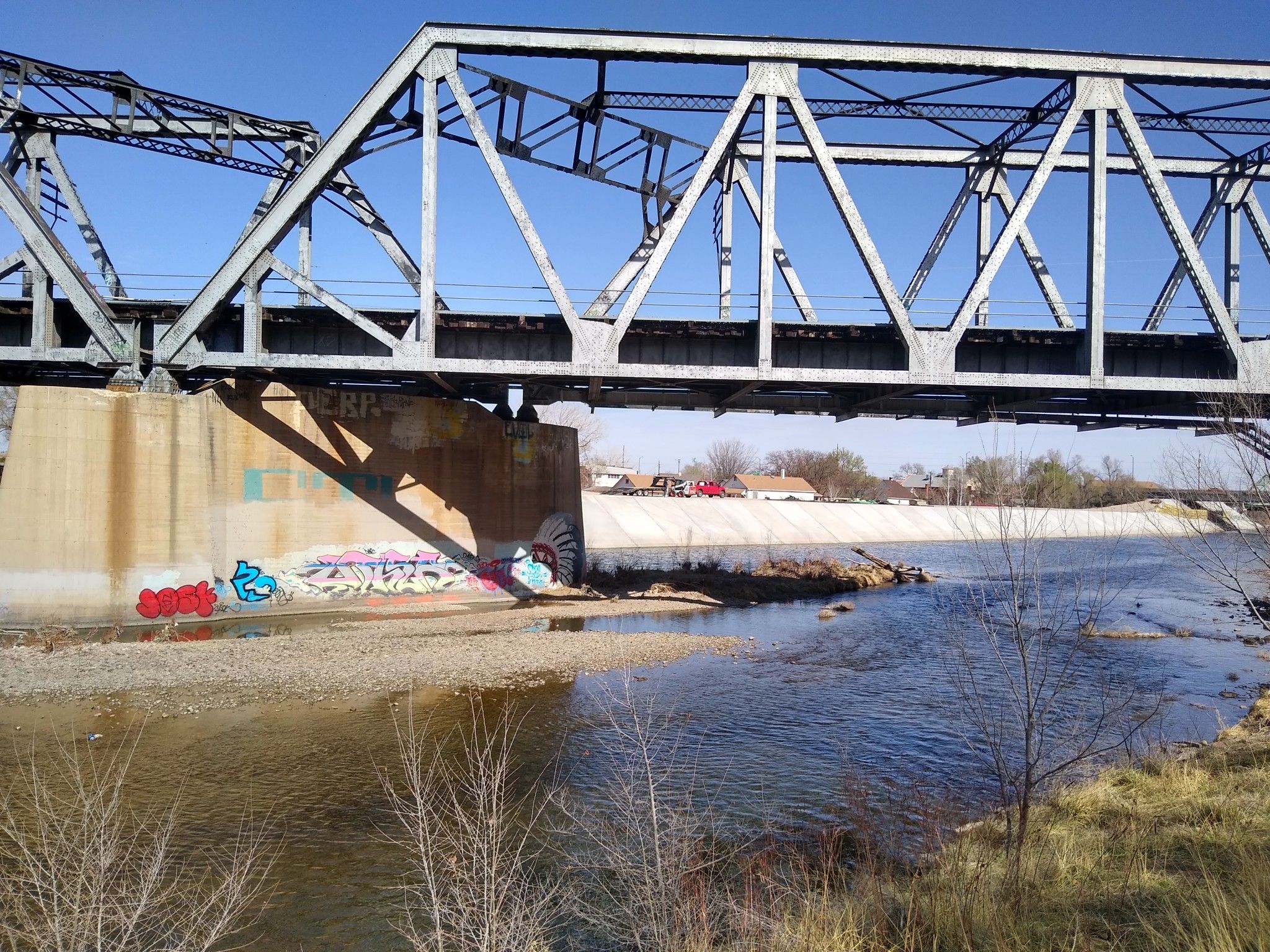 A metal truss bridge spans a river on a bright, sunny day. - Pueblo to Beulah loop