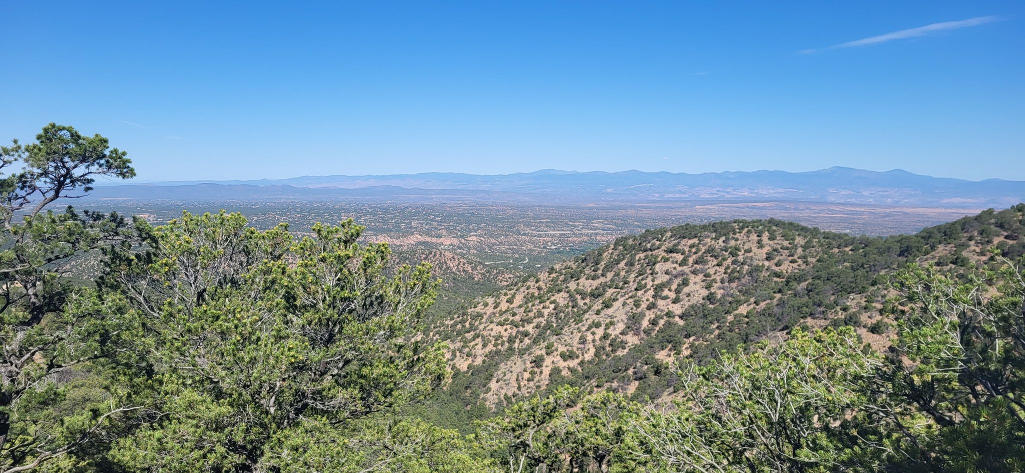 Expansive view of a green valley and distant mountains under a clear blue sky. - Chamisa, Saddleback, Juan, and Winsor Trail loop