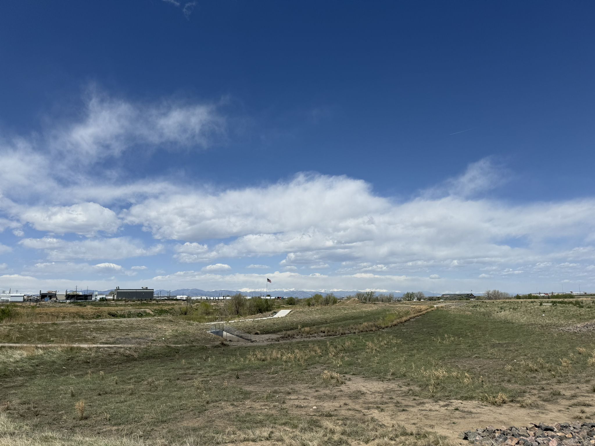 Wide open grassy field with a path, distant buildings, and a bright cloudy sky. - View of Sand Creek – Central Park loop from Former Stapleton Airport Control Tower