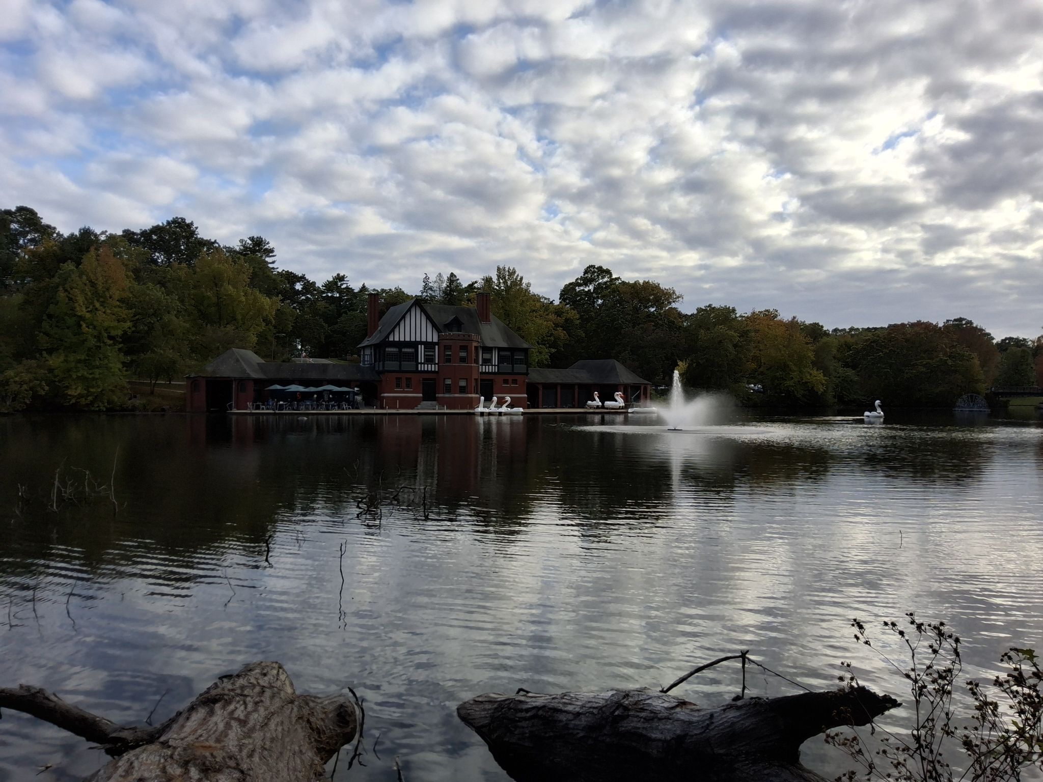 A large building and fountain on a lake with swan boats under cloudy skies. - Big Lakes Trail
