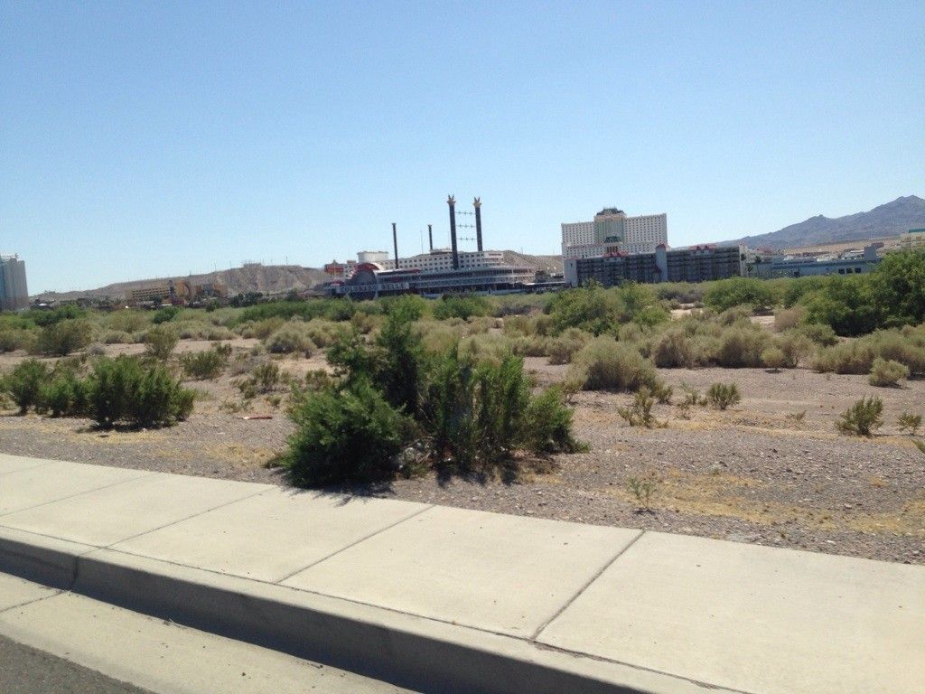 Dry desert landscape with scrub brush and distant buildings under a clear sky. - Bullhead City and Davis Dam loop