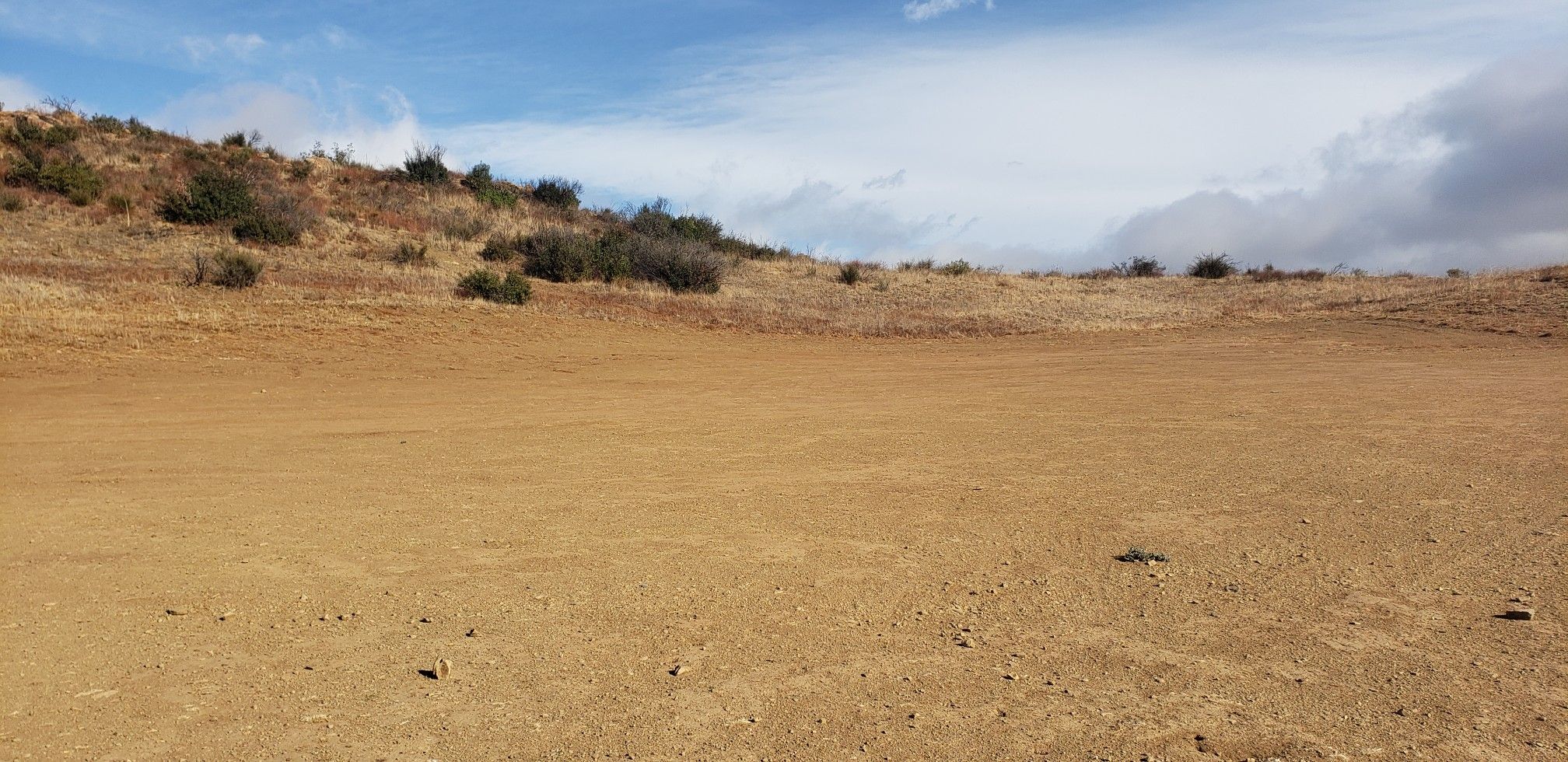 An empty dirt field with dry, brush-covered hills under a cloudy sky. - China Flat and Albertson Motorway Loop