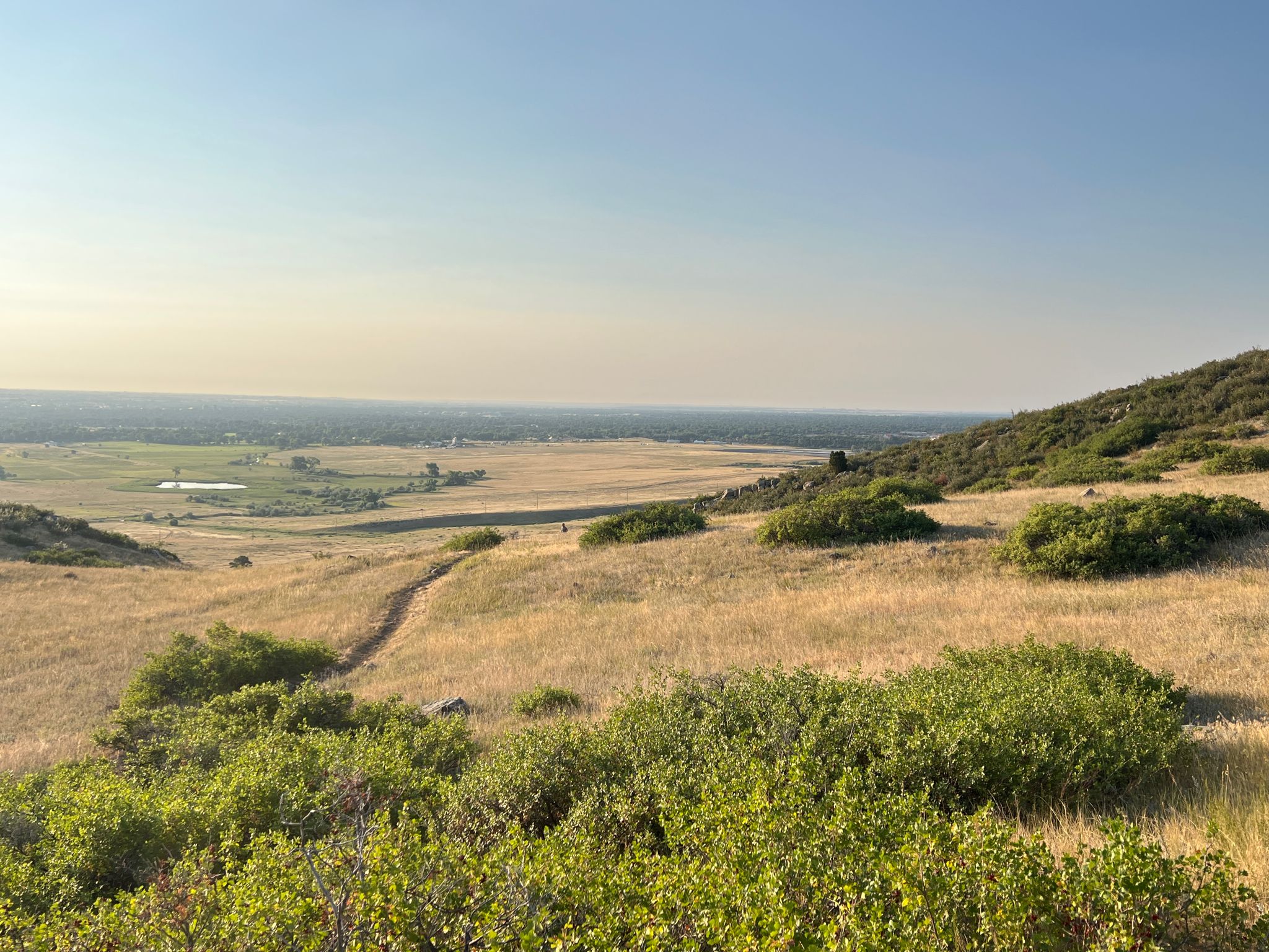 Winding dirt trail through golden grassy hills with a hazy distant valley. - Foothills and North Loop Trail