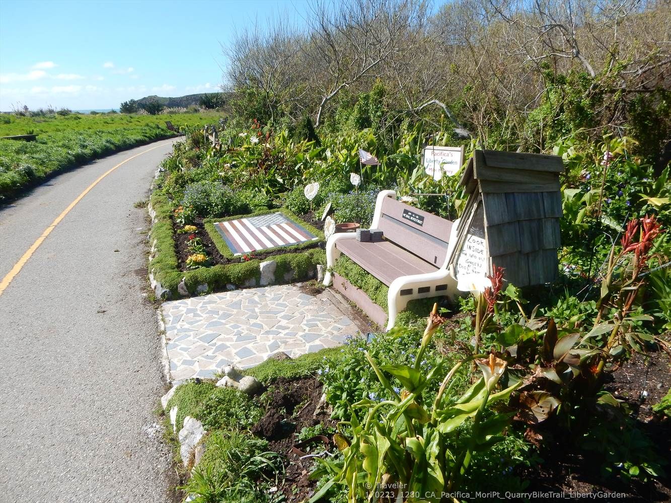 A park bench and garden next to a paved path on a sunny day. - Coastal Lookout via Mike's Garden