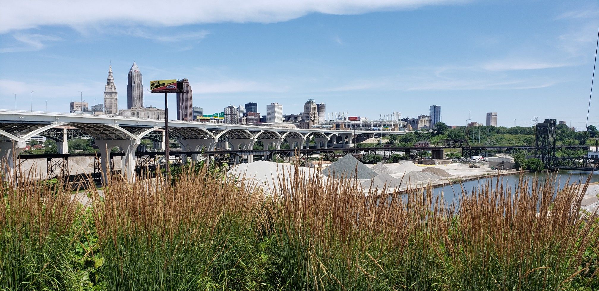 City skyline, arched bridge, and industrial riverfront under a bright sky. - Ohio & Erie Canal Reservation – West Side Market loop from West 65th–Lorain (Eco-Village)