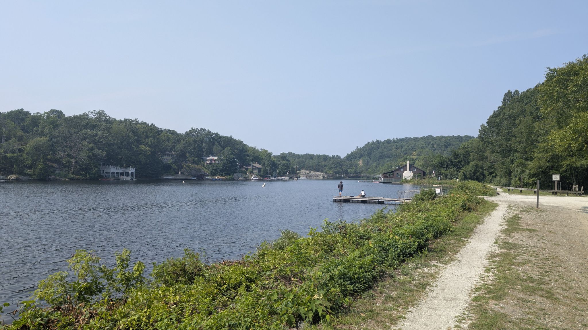 Wide lake with distant buildings, two people on a dock, bright day. - Waving Willie Loop