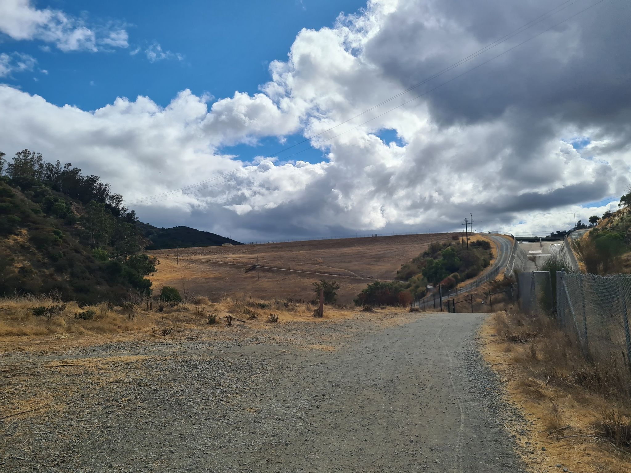 A wide gravel path leading to open fields under a dramatic cloudy sky. - Lexington Reservoir – Los Gatos Creek Trail loop from Los Gatos