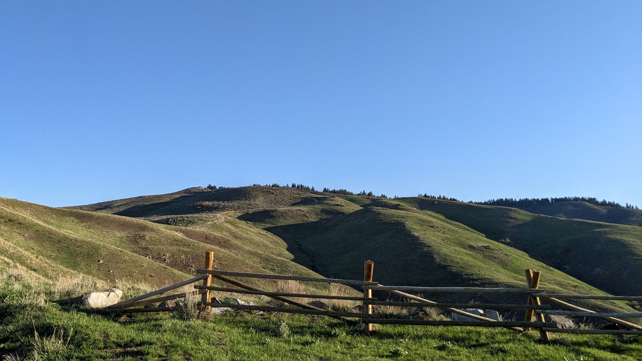 Wooden fence in foreground with sunny, green rolling hills under clear sky. - Shaw Mountain Road and Homestead Trail Loop