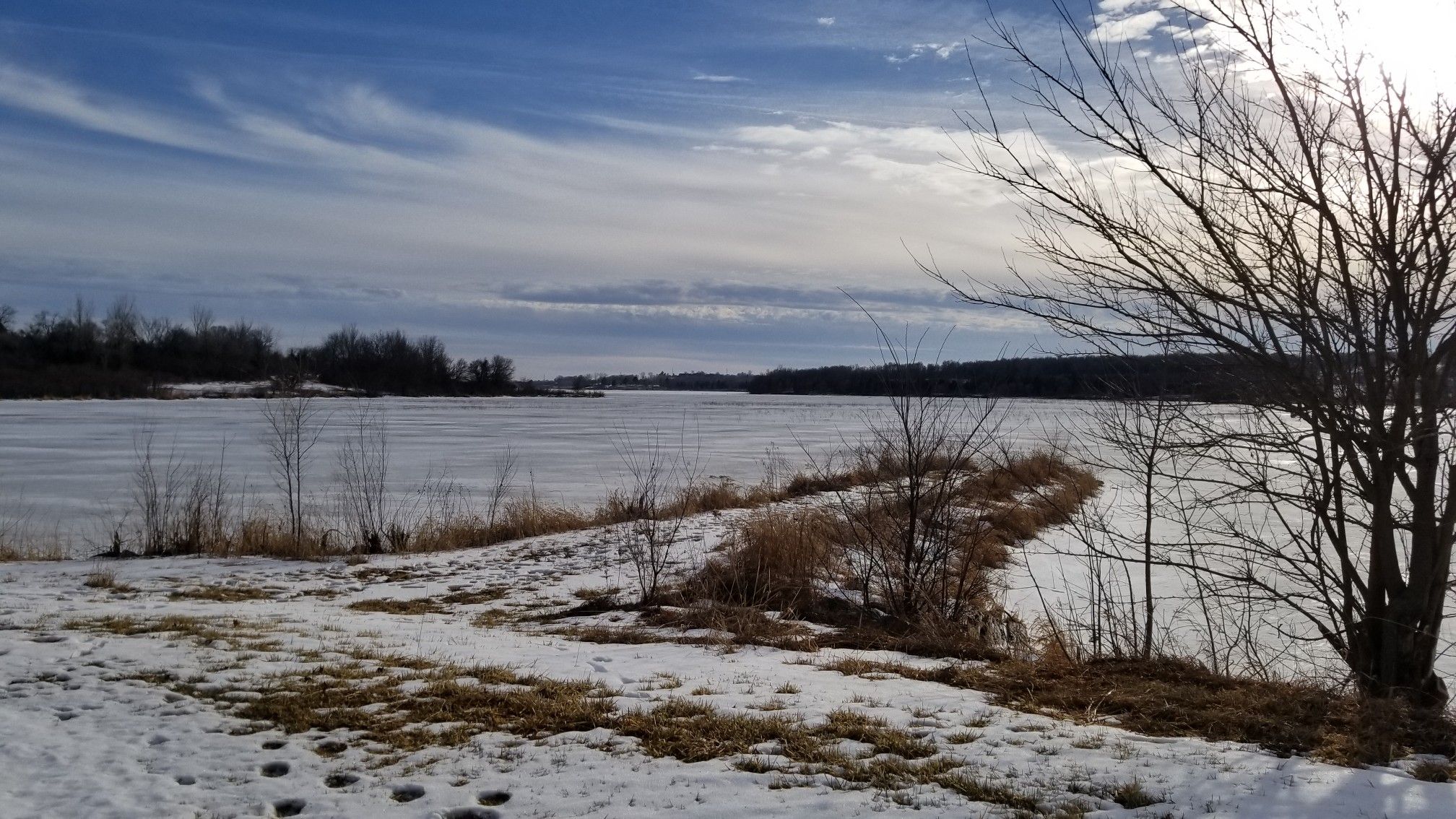 Frozen lake with snow-covered banks and bare trees under a cloudy winter sky. - Cunningham Lake Pavilion – Glenn Cunningham Lake loop from Glenn Cunningham Lake Park