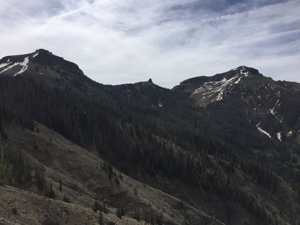 Dark, forested mountain peaks with snow patches under a cloudy sky. - Quartz Lake Trail