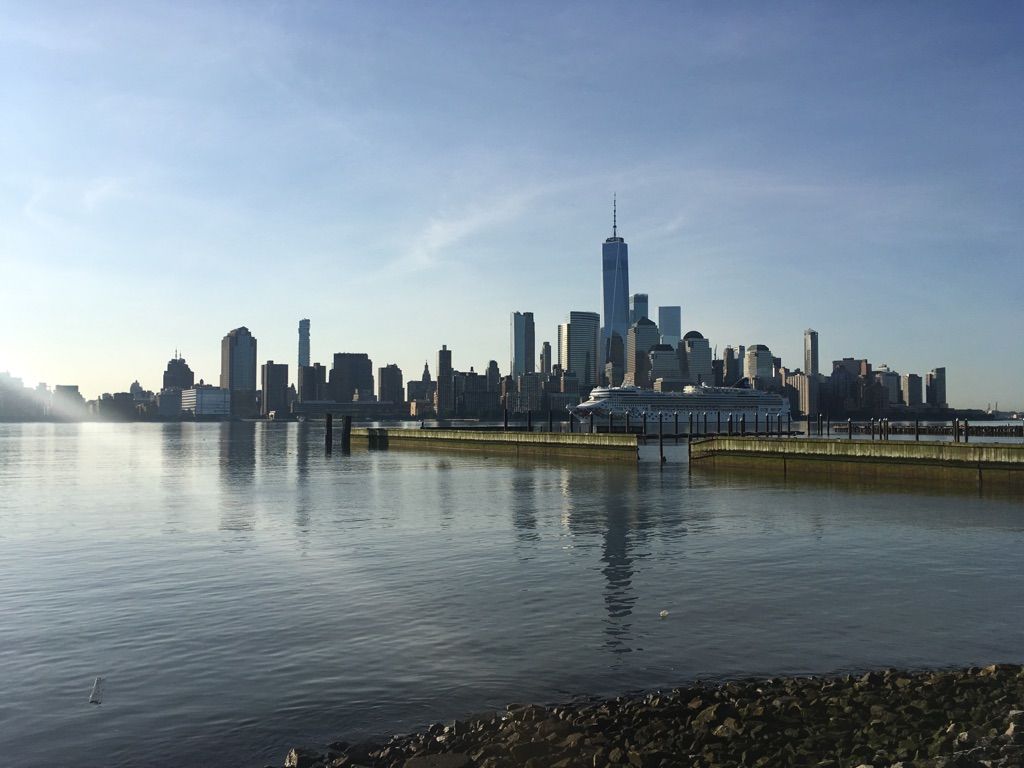 City skyline across water with a pier, under bright morning light. - LeFrak Point Lighthouse – Hoboken Newport Walkway loop from Grove Street