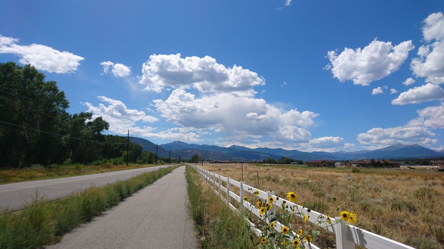 A road and path beside a white fence, with distant mountains under a blue sky. - Salida and Poncha Springs loop
