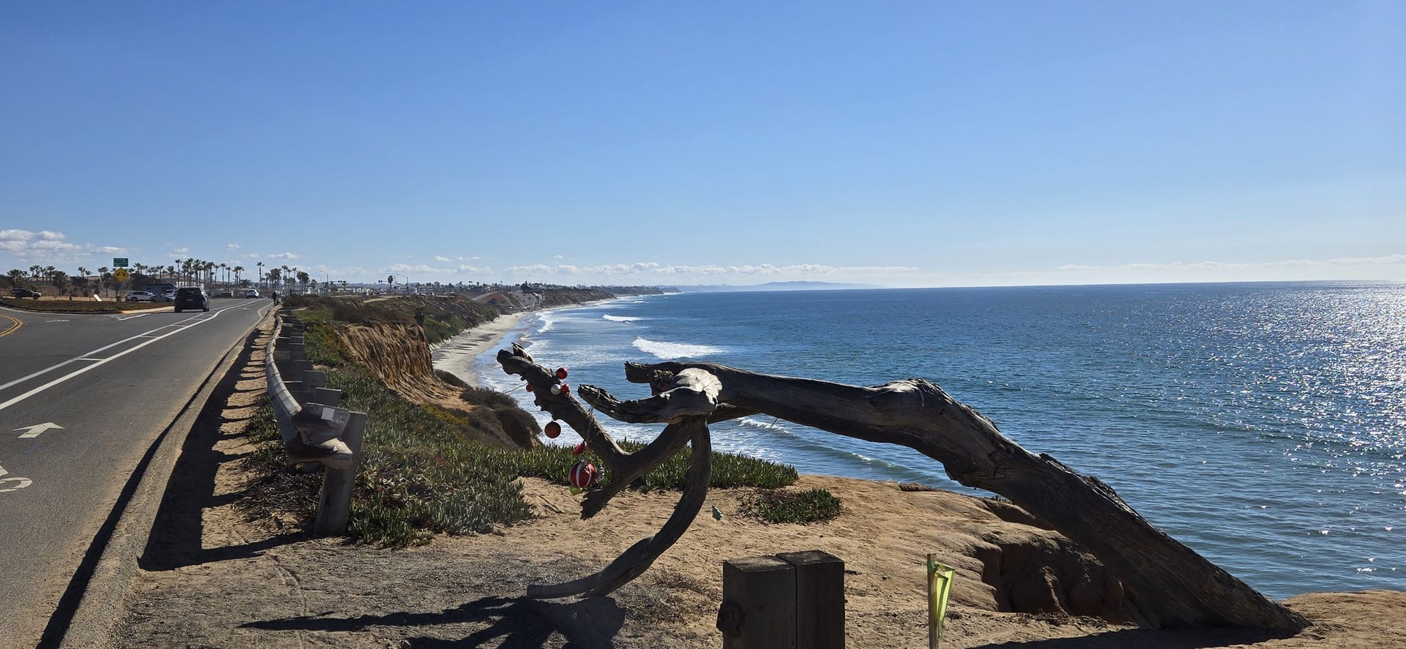 Sunny coastal road beside ocean waves, with a large driftwood sculpture. - California Mission Trail - stage 01 Mission San Diego de Alcalá (1769) to Mission San Luis Rey (1798)
