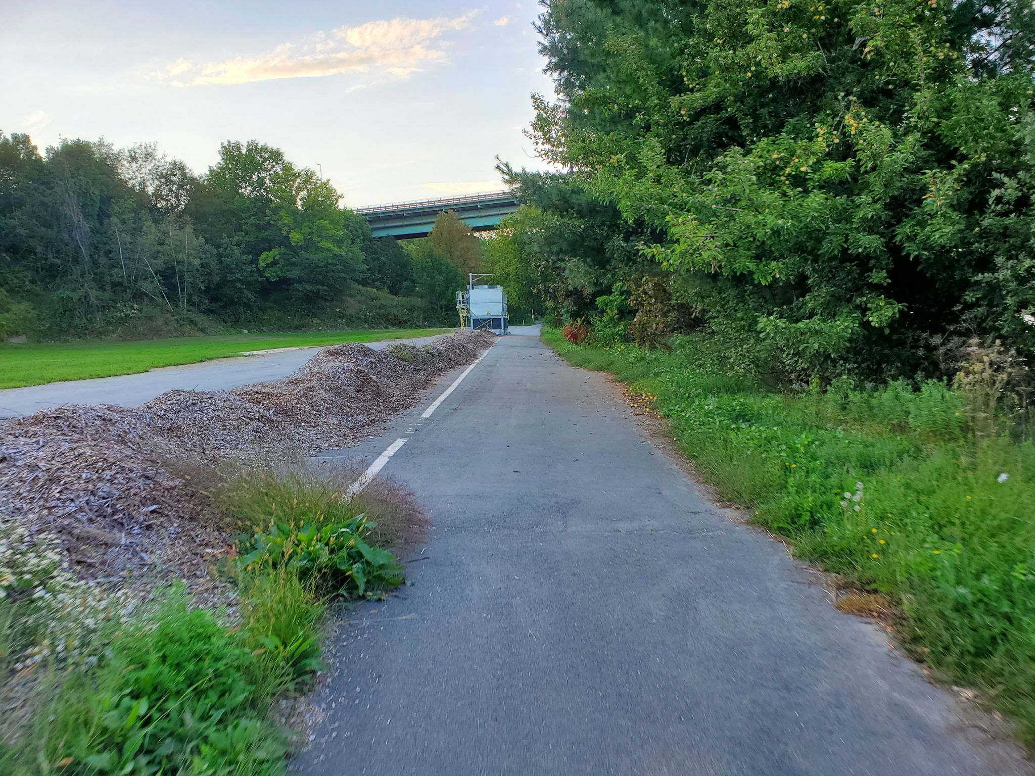Paved path next to a large gravel pile, with trees and a distant bridge. - Start of Hawthorne Hike – Belfast Rail Trail loop from Belfast