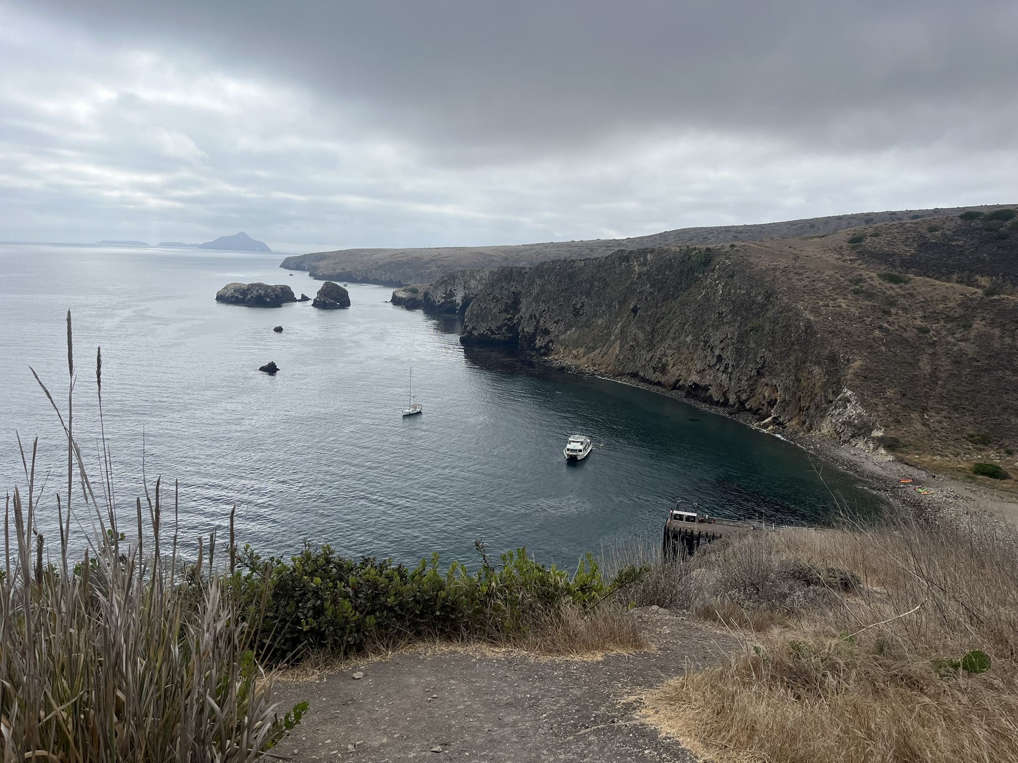 Overcast view of a gray bay with a boat and rocky cliffs. - Lower Scorpion Campground – Cavern Point loop from Channel Islands Adventure Company