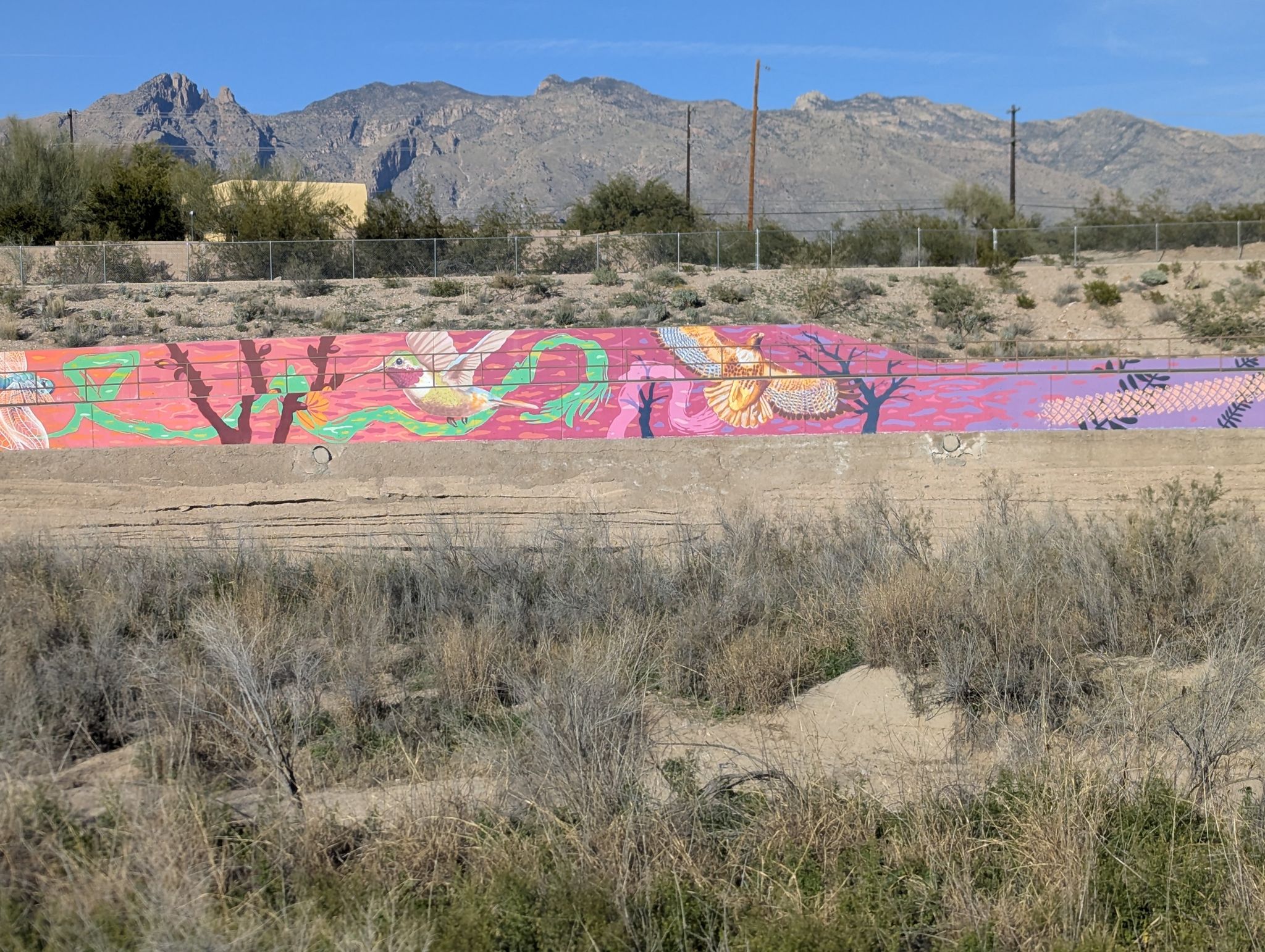 Colorful mural on a wall in a dry landscape, with mountains in the background. - Towers of a Martian Odyssey – Nature of Movement loop from Skyline Gateway