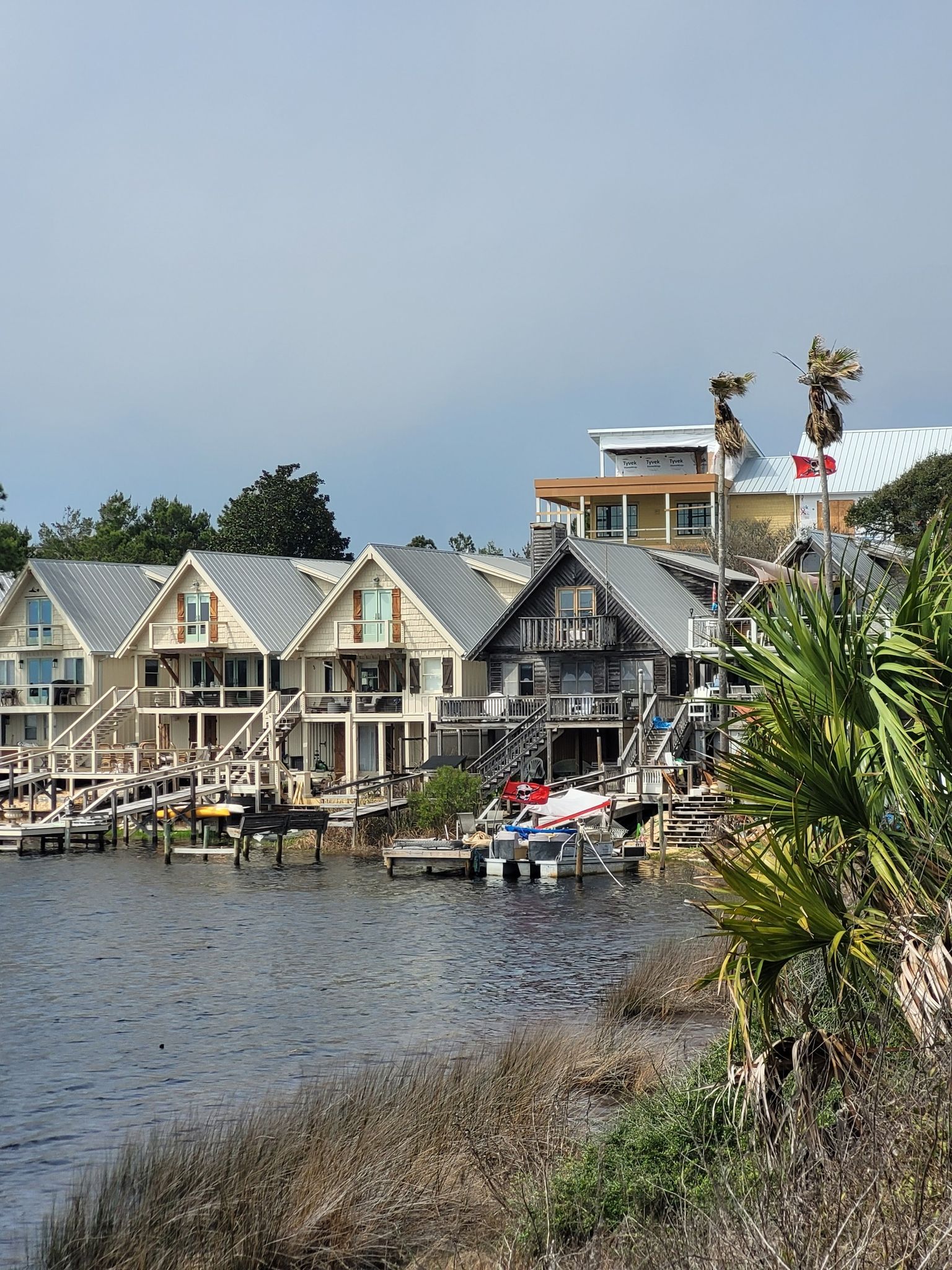 Waterfront houses with docks and palm trees under an overcast sky. - Timpoochee Trail – Eastern Lake loop from Rosemary Beach