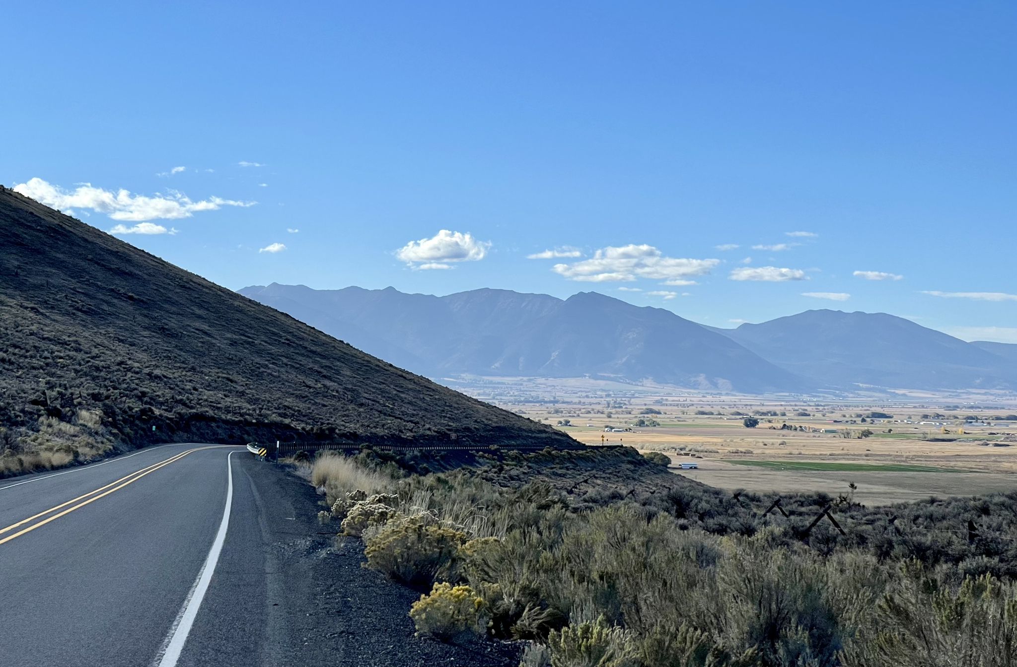 A winding road alongside a dry hillside overlooking a valley and distant mountains. - Historic Baker loop