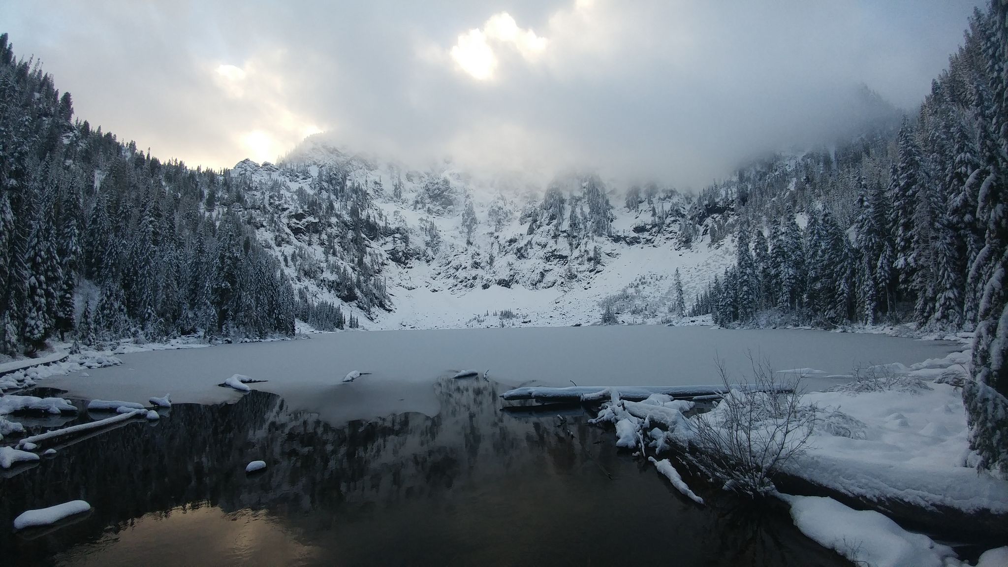 Partially frozen lake surrounded by snow-covered mountains under a cloudy sky. - Lake Twenty Two Trail
