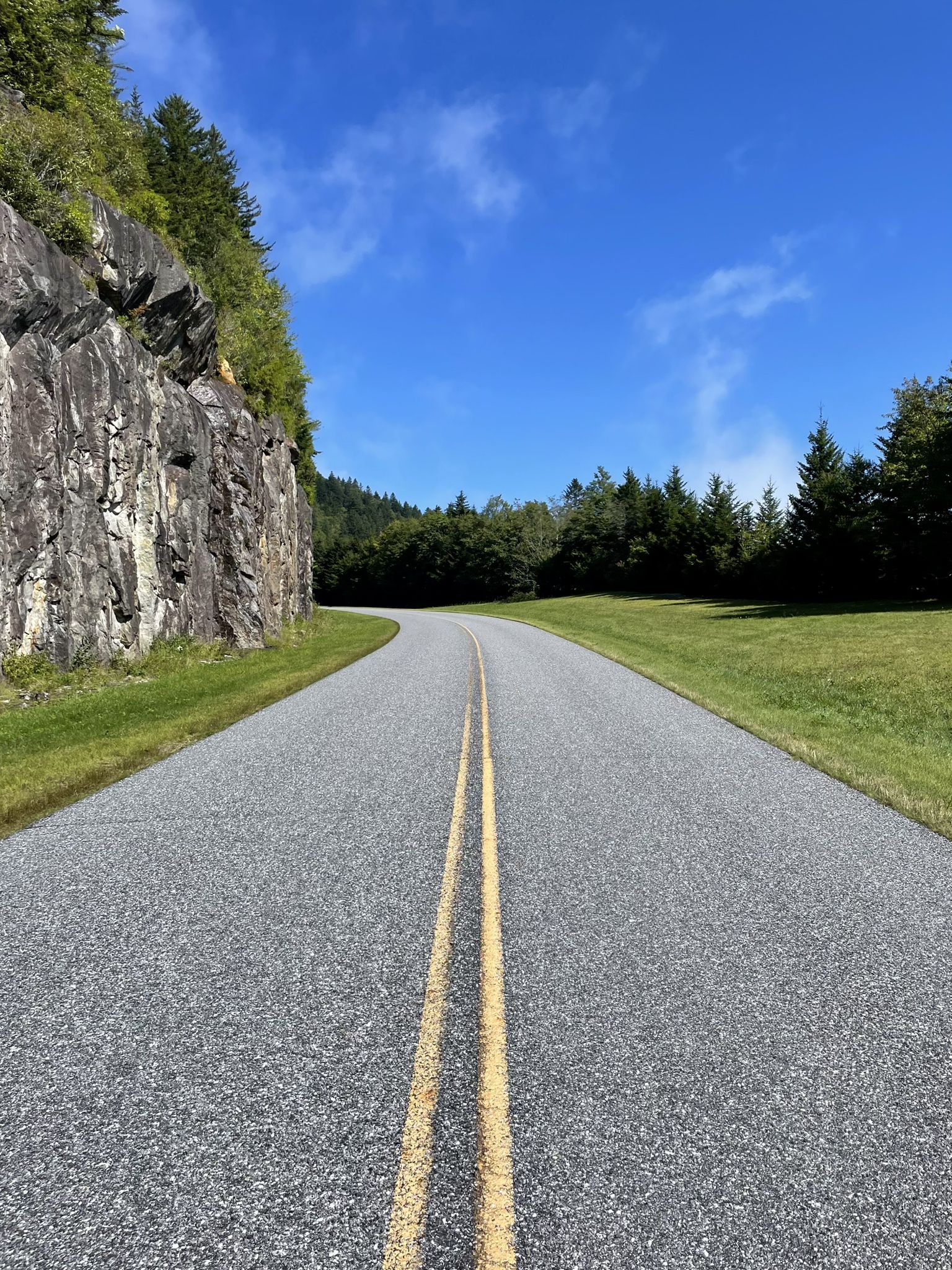 Winding paved road next to a rock face under a clear blue sky. - Richland Balsam loop