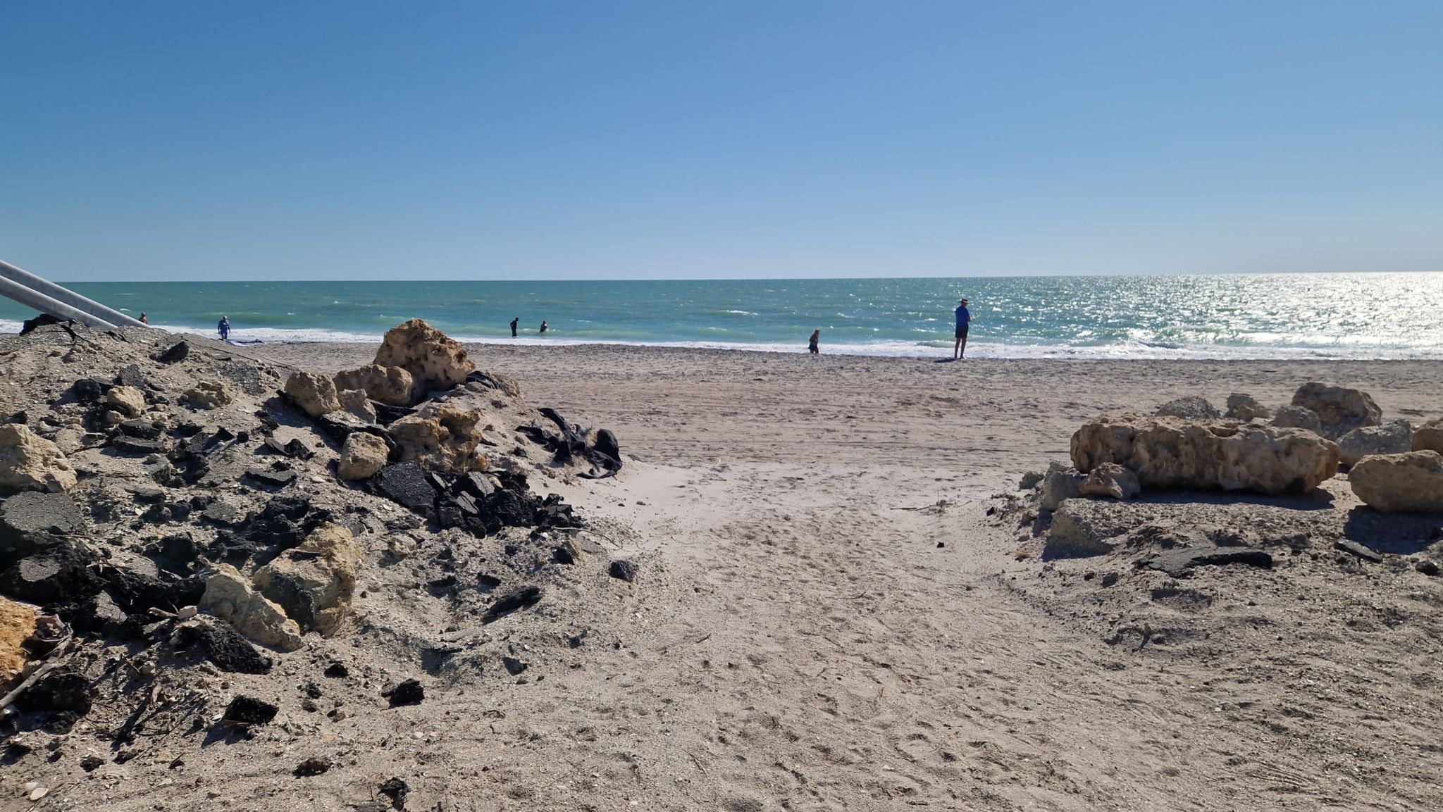 Sandy beach with people near the ocean under a clear sky. - Manasota Key