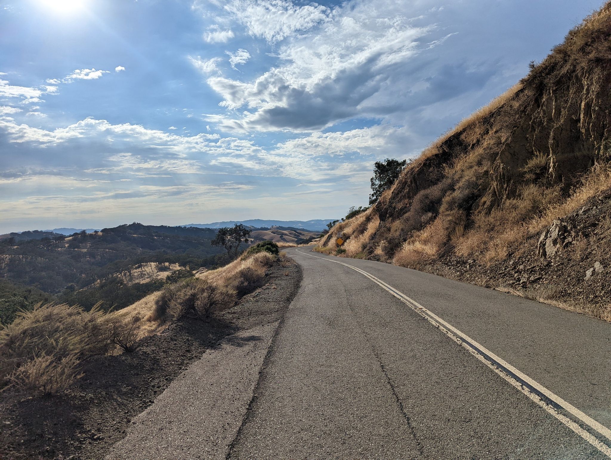 Winding road alongside a dry hillside under a partly cloudy sky. - Livermore Valley Overlook loop from Diablo Foothills Regional Park
