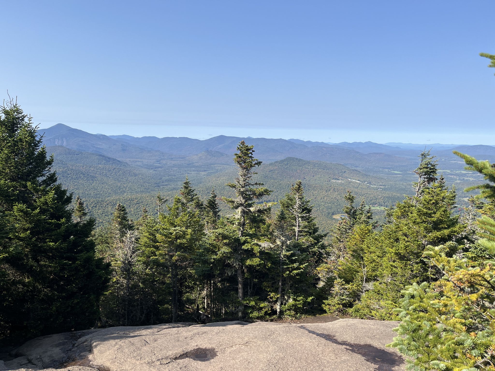 Panoramic view of distant mountains over a dense evergreen forest. - Cascade Mountain Trail