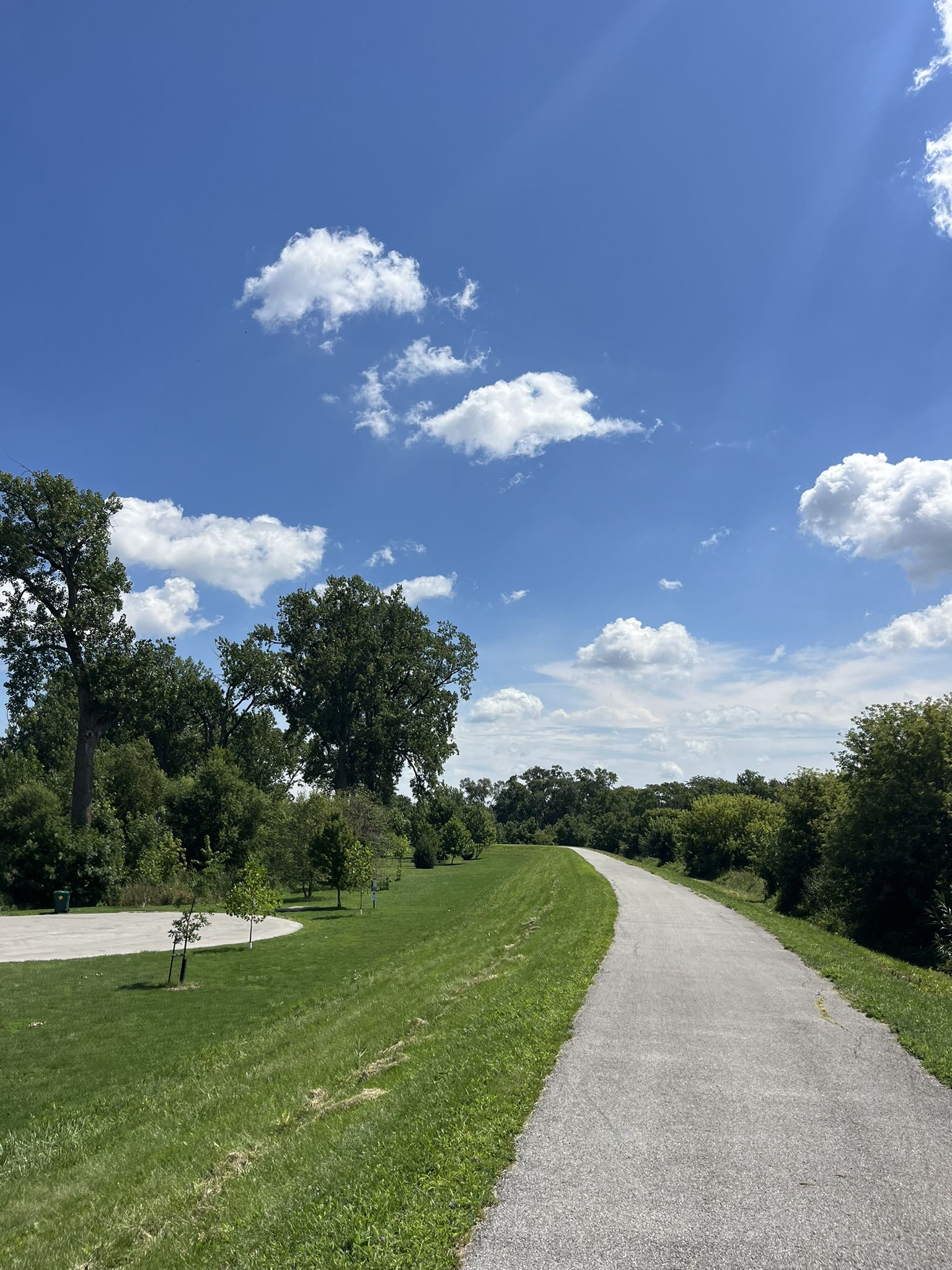 Paved path winding through green grass and trees under a sunny sky. - Monon Trail loop from Lansing